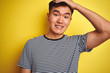 © Krakenimages.com - Young asian chinese man wearing striped t-shirt standing over isolated yellow background stressed with hand on head, shocked with shame and surprise face, angry and frustrated. Fear and upset