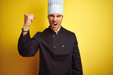 Sticker - Young chef man wearing uniform and hat standing over isolated yellow background angry and mad raising fist frustrated and furious while shouting with anger. Rage and aggressive concept.