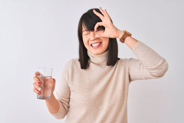 Young beautiful Chinese woman holding glass of water over isolated white background with happy face smiling doing ok sign with hand on eye looking through fingers