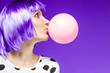 canvas print picture - Beautiful girl in violet wig is blowing a huge pink bubble with bubblegum. Stylish fashion woman dressed in blouse with polka dots. Bright young female on purple background. Fun and gladness concept.