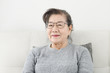 © nuiiko - Happy Asian senior woman wearing eyeglasses and sitting on sofa at home, lifestyle concept.