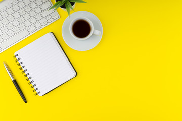 Flat lay view of office table desk. Workspace with keyboard, pen, book, coffee and decoration flower on yellow background. Copy Space concept