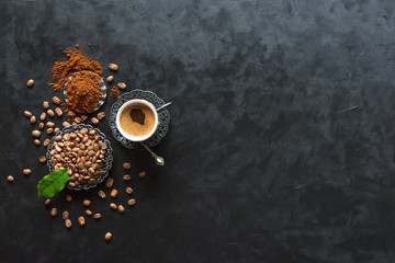 Cup of coffee and coffee beans with ground powder on black background, top view