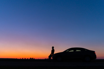 silhouette of a man and a car on a background of a very beautiful sunset. freedom and travel by car 