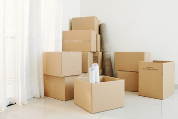 Many opened and closed cardboard boxes in corner of empty room of new house