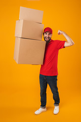 Full length portrait of joyful delivery man in red uniform smiling while carrying packaging boxes