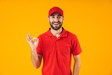 Wall Mural - Portrait of happy delivery man in red t-shirt and cap smiling and showing ok sign