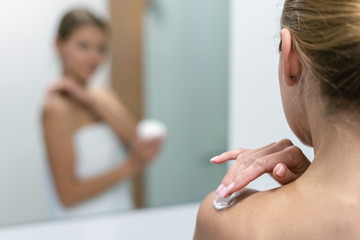 Wall Mural - Woman applying body cream on shoulder in bathroom