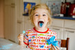 © Irina Schmidt - Gorgeous little toddler girl licking lollypops and showing colored blue tongue. Funny child having fun with coloring bonbon, indoors