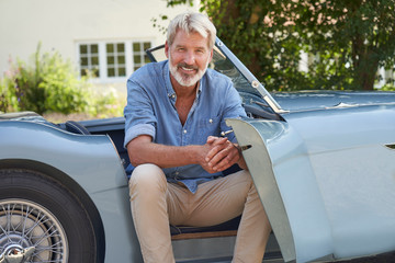 portrait of proud mature man sitting in restored classic sports car outdoors at home