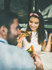 Young happy caucasian couple sitting at table eating pizza in Italian cuisine cafe on sunny summer day