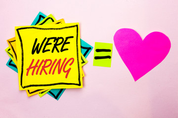 Text sign showing We're Hiring. Conceptual photo Recruiting Hiring Now Recruitment Vacancy Announced Hire written Yellow Sticky Note Paper the plain background Pink Heart next to it.