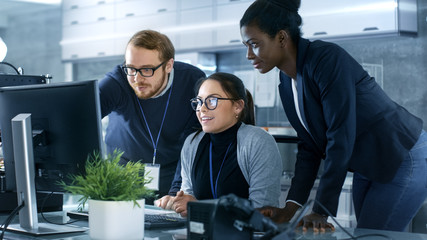 Diverse Team of Scientific Engineers Doing Research on a Computer in a high Tech Laboratory on a High Profile Start-up. Team Consists of Black and Caucasian Young Women and White Male.