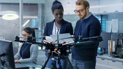 Wall Mural - caucasian male and black female engineers working on a drone project with help of laptop and taking 