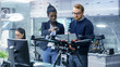 © Gorodenkoff - Caucasian Male and Black Female Engineers Working on a Drone Project with Help of Laptop and Taking Notes. He Works in a Bright Modern High-Tech Laboratory.