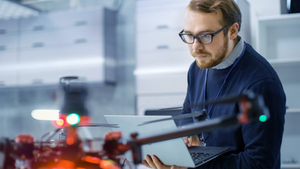 Wall Mural - male engineer programs drone while holding laptop in his hands. he works in a bright modern high-tec