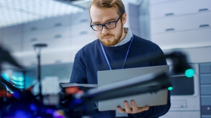 Wall Mural - young male engineer programs drone while holding laptop in his hands. he works in a bright modern hi