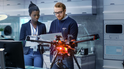 Wall Mural - caucasian male and black female engineers working on a drone project with help of laptop and taking 