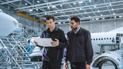 Wall Mural - Team of Aircraft Maintenance Mechanics Moving through Hangar. Holding Tablet Computer