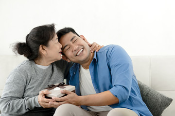 Wall Mural - Happy Asian man giving gift box to his mother for Mother's Day celebration.