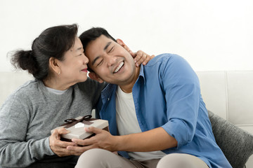 Wall Mural - Happy Asian man giving gift box to his mother for Mother's Day celebration.