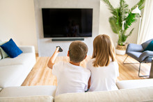 A Two Family Brother And Sister Holding Remote Control And Watching TV Show. Back View