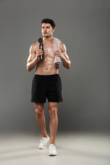 Poster - Handsome young strong sportsman isolated over grey wall background holding towel and bottle with water.