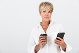 Fototapeta Uliczki - Portrait of attractive adult woman with short blond hair holding cellphone and takeaway coffee cup