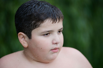 closeup portrait of small fat caucasian boy on green plant background outdoor leisure