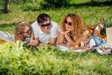 Family picnic on grass in the gardens under gentle shade of trees