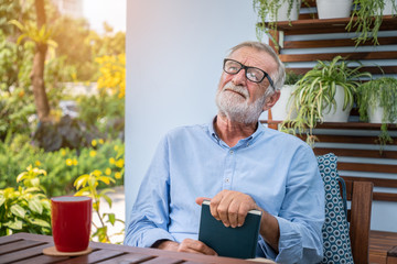 Senior elderly man holding book in hand with mug of coffee in garden