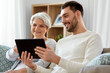 © Syda Productions - family, generation and technology concept - happy smiling senior mother and adult son with tablet computer at home