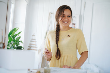 Young cheerful woman with braid painting with brush on wooden tray.