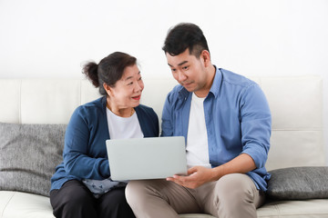 Wall Mural - Asian young man and senior woman using laptop computer in living room concept Son teach mother use computer laptop