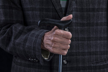 hands of an old man with a crutch on a black background