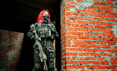 Airsoft red-hair woman in uniform with machine gun standing on ruins. Horizontal photo