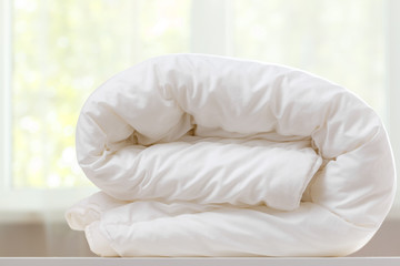 a folded white duvet lies on a table on a blurred background.