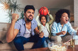 © Mediteraneo - Happy African American family of three watching tv and cheering sport games on sofa at home