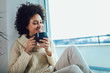 © Mediteraneo - African American woman in her living room drinking holding a coffee tea mug