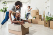 © lordn - Happy playful  African American family moving in new apartment, little preschooler daughter sitting in cardboard boxes, father rolling her,  purchase property concept