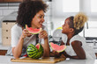 © lordn - Beautiful African Mother and Daughter eating Watermelon at Home Kitchen