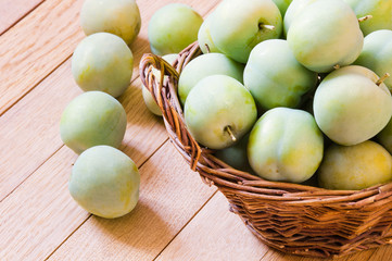 Wall Mural - Ripe yellow-green plums in a wicker basket on a wooden table