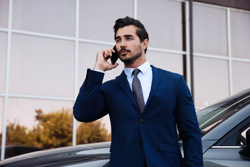 Attractive young man talking on phone near luxury car outdoors