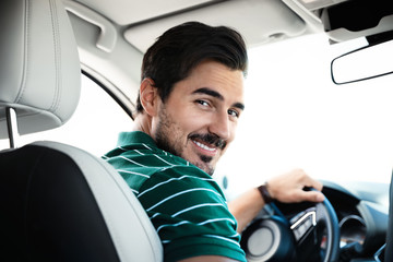 Attractive young man driving luxury car, view from backseat