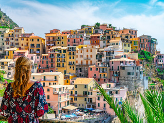 Young woman with red hair watching the amazing view of Manarola village in Cinque Terre, Italy. Sunny day and blue sky of an afternoon in the European summer. Unesco World Heritage Site