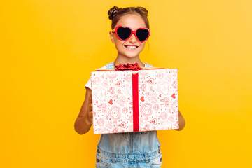 Wall Mural - Shocked young girl, a teenager holds a gift box in hand, standing on a yellow background