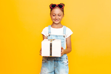 Wall Mural - Shocked young girl, a teenager holds a gift box in hand, standing on a yellow background