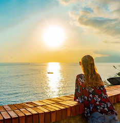 Young woman watching the sunset over the Mediterranean sea. Blue sky and little boat.