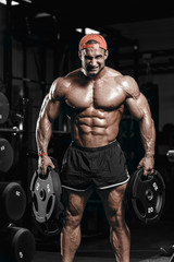 Wall Mural - Muscular athletic bodybuilder man hard training in gym over dark background with dramatic light with weights in strong pumped hands