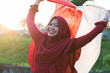 © SVRSLYIMAGES - portrait of young asian muslim woman with scarf lift the red and white flag into the air
